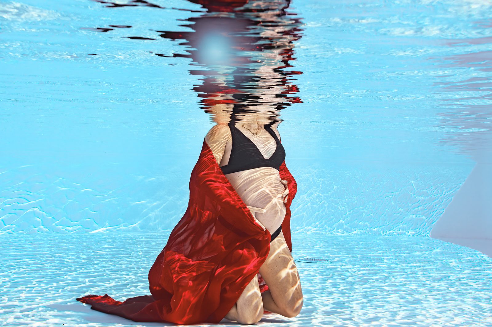 Séance photo grossesse aquatique en piscine, voile rouge flottant